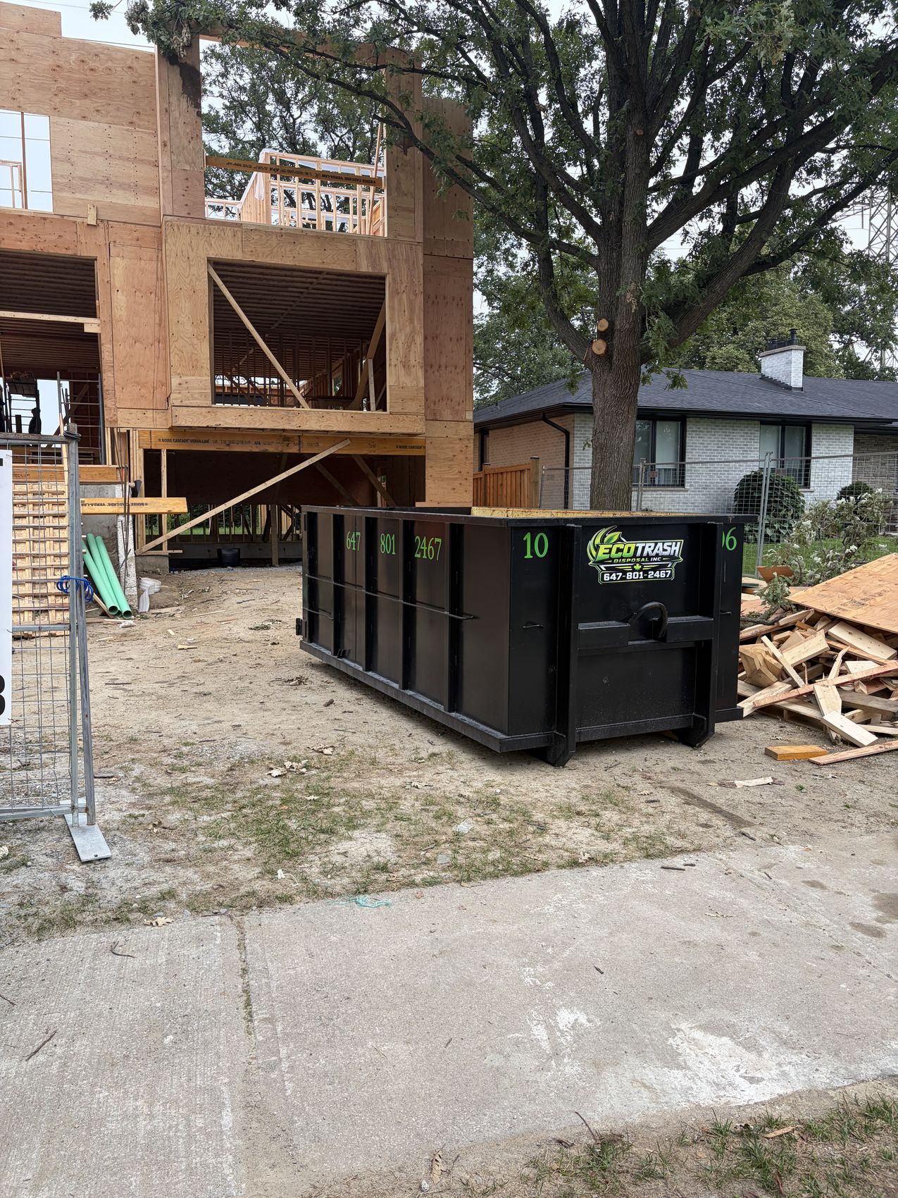 Black Eco Trash bin beside a house under construction with lumber debris