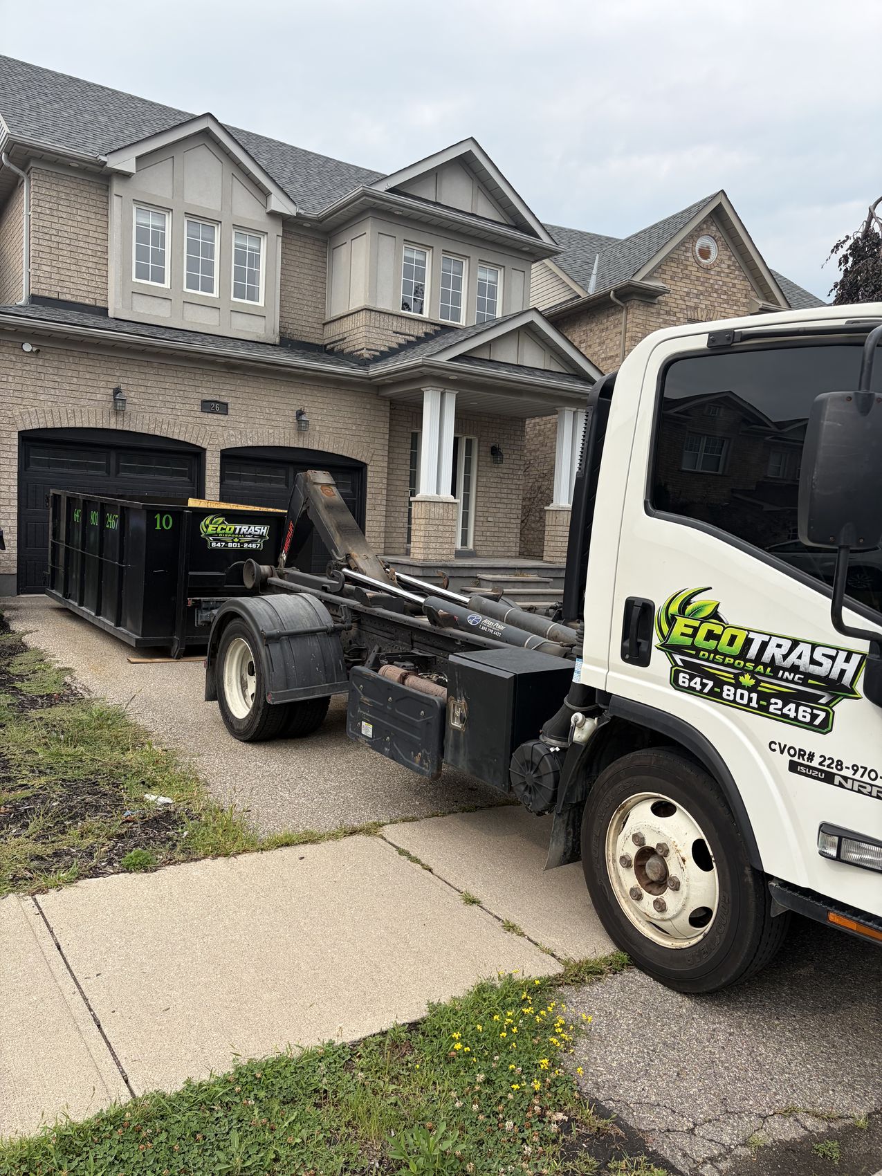 Eco Trash hook lift truck delivering a black bin to a suburban home