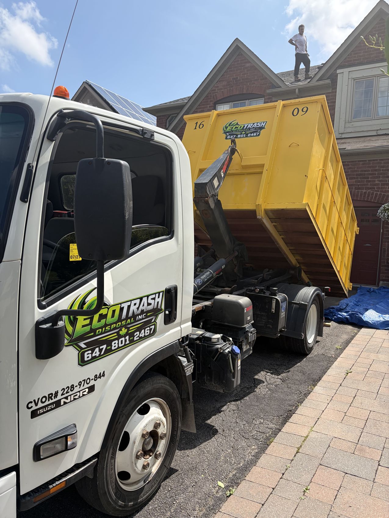 Eco Trash truck lifting a loaded yellow bin at a roofing job